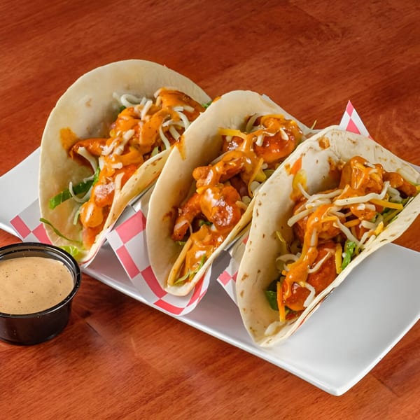 Three Al Tacos Locos shrimp tacos with sauce and cheese, served with a side of dipping sauce.