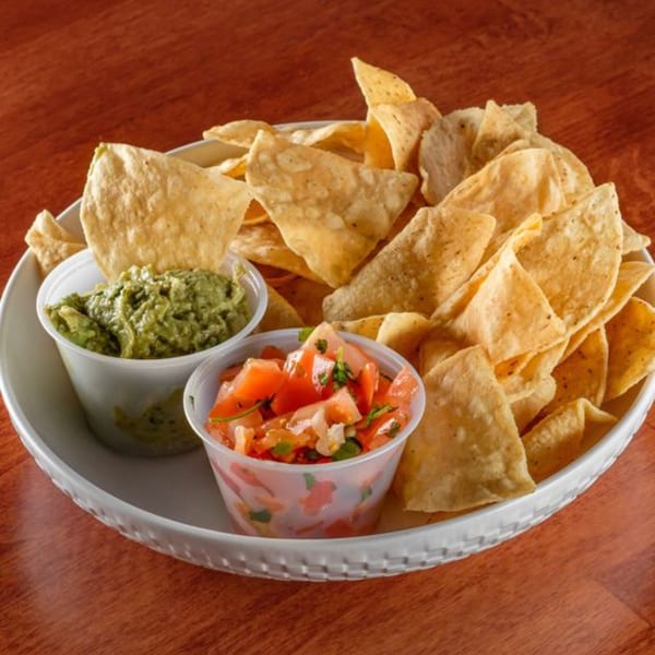 A white plate filled with tortilla chips, guacamole, and pico de gallo on a wooden table.