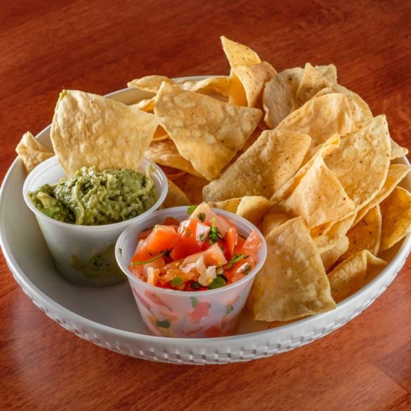 A white plate filled with tortilla chips, guacamole, and pico de gallo on a wooden table.