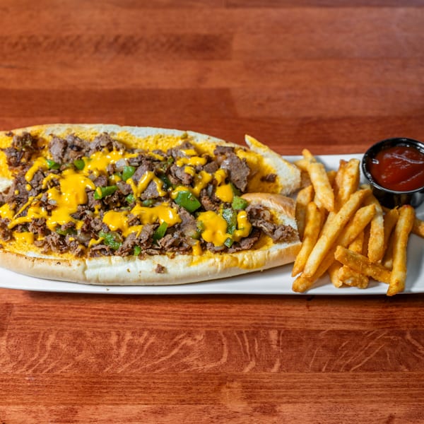 Cheesesteak with melted cheese, green peppers, and onions, served with fries and ketchup.