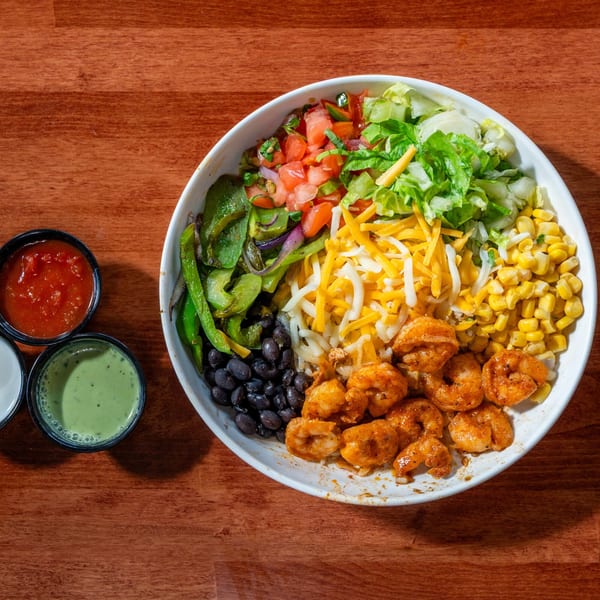 A vibrant shrimp burrito bowl with rice, beans, corn, cheese, lettuce, and salsa on a wooden table.