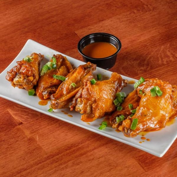 Al Tacos Locos' spicy chicken wings with green onions and a side of dipping sauce.