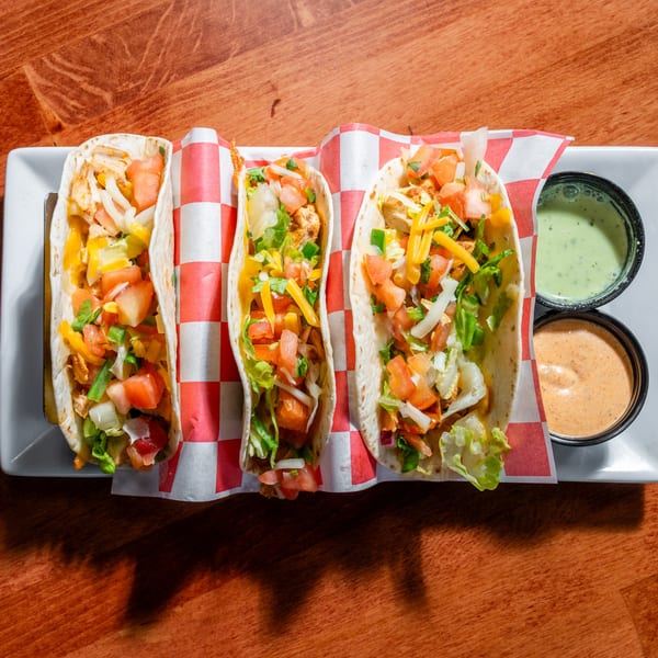 Three Al Tacos Locos chicken tacos with fresh toppings and two dipping sauces on a white plate.