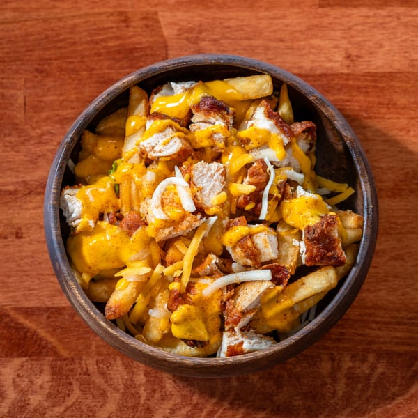 Al Tacos Locos' Mexican fries topped with chicken, melted cheese, and white onions in a wooden bowl.