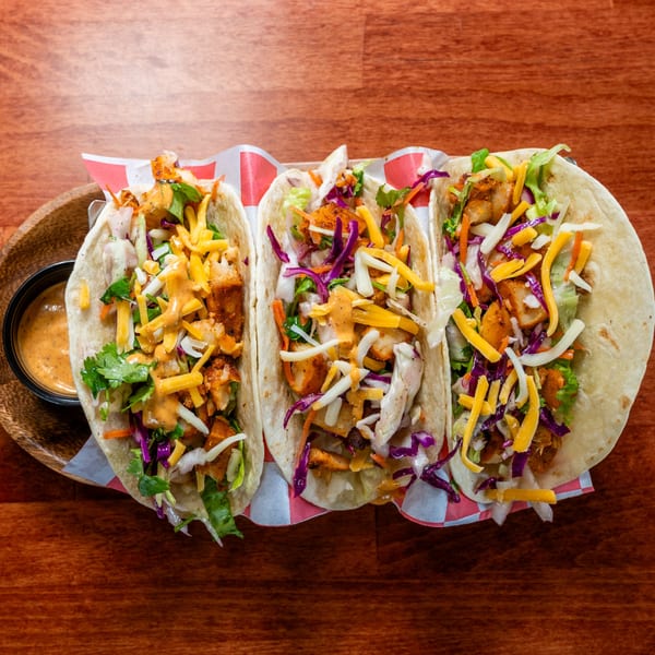 Three Al Tacos Locos tacos with chicken, cheese, cabbage, and sauce, on a wooden table.